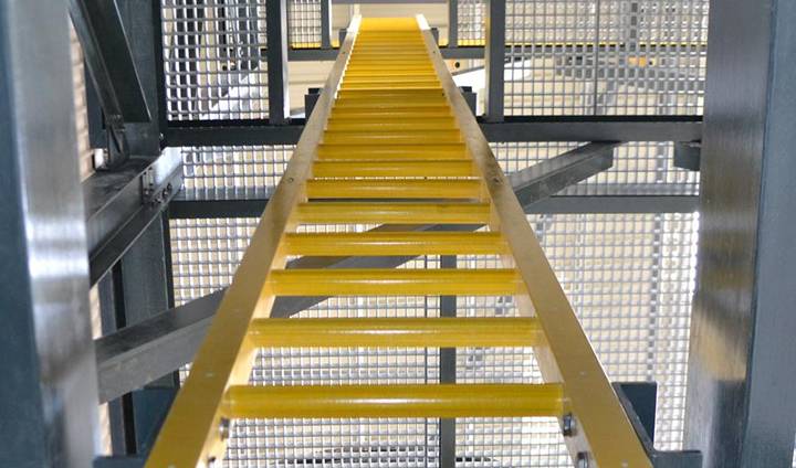 A yellow fixed ladder is mounted on the frames of factory structure.